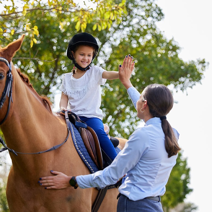 Young girl on a brown horse with her instructor
